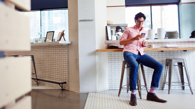 Man seated at café counter checking his phone.