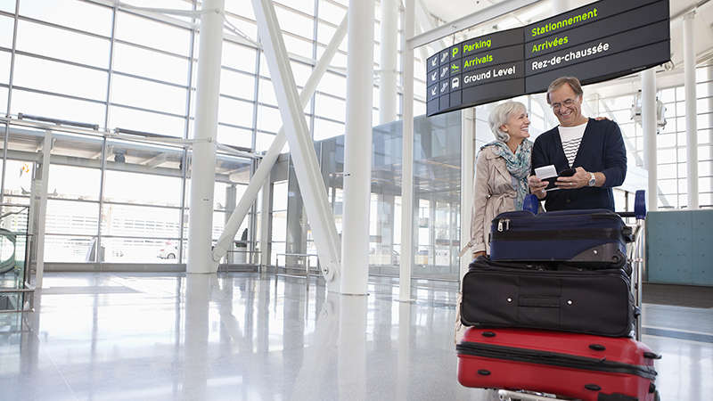 Smiling couple with full luggage trolley in airport.